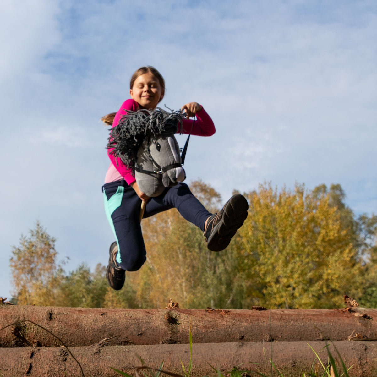Kind springt mit Hobby Horse Grauschimmel über ein Hindernis